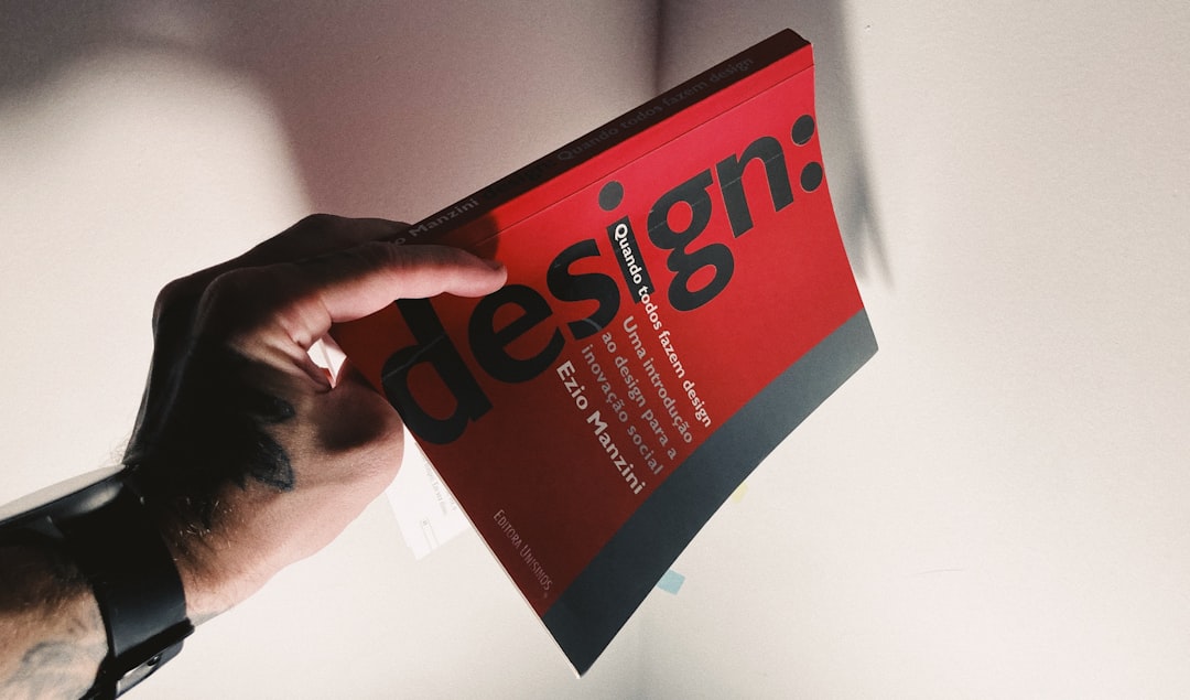 home-hero Tattooed hand holding a red book about design.